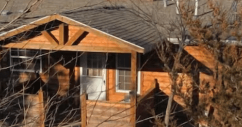 A wooden house with a porch, surrounded by bare trees and a clear sky.