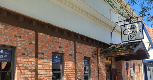 Exterior of a brick building featuring a sign that reads "Crown and Rye," with storefront windows below.