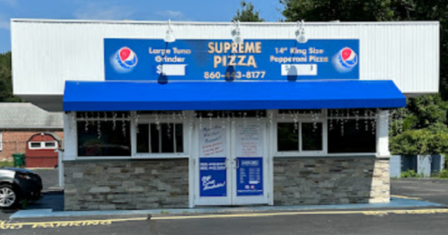 A pizza shop with a blue awning and signage, featuring "Supreme Pizza" and a phone number, set in a sunny outdoor area.
