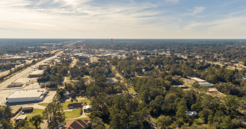 Aerial view of a small town with roads, buildings, and trees under a clear sky.