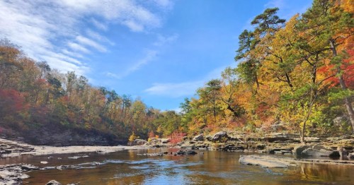 A serene river scene surrounded by colorful autumn foliage and rocky banks under a clear blue sky.