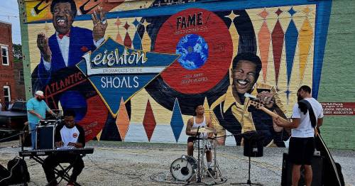 Musicians perform in front of a colorful mural celebrating the history of music in Muscle Shoals, Alabama.