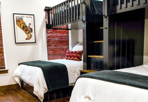 A cozy bedroom featuring a lofted bed, a lower twin bed, and decorative pillows, with wooden accents and warm lighting.