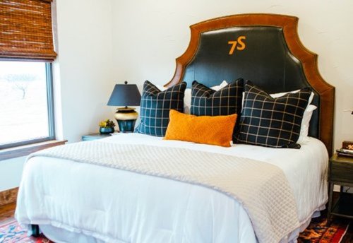 Cozy bedroom featuring a stylish bed with decorative pillows, a bedside lamp, and a window with wooden blinds.