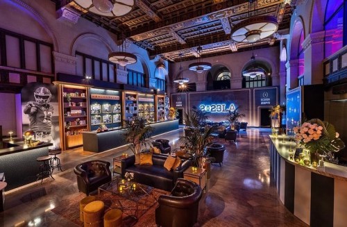 A stylish event space with elegant decor, featuring leather seating, plants, and a large illuminated backdrop.