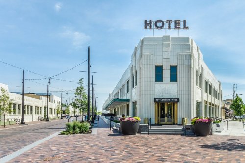 Art Deco hotel building with "HOTEL" sign, surrounded by greenery and a brick walkway, under a clear blue sky.