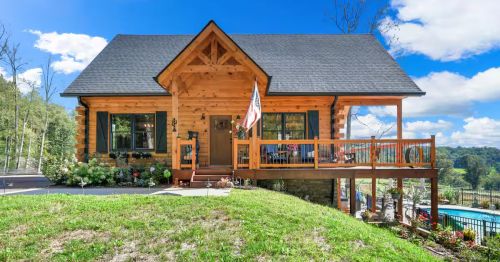 A wooden log cabin on top of a hill with a pool and hot tub off to the side in Maryland