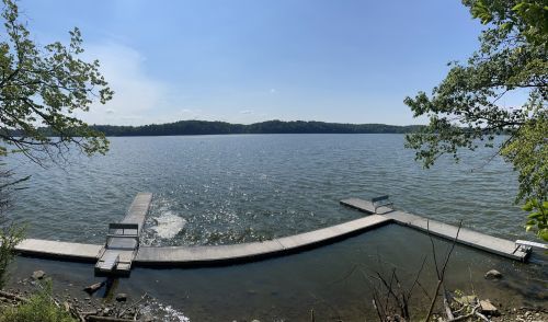 A serene lake view with two docks extending into the water, surrounded by trees and a clear blue sky.