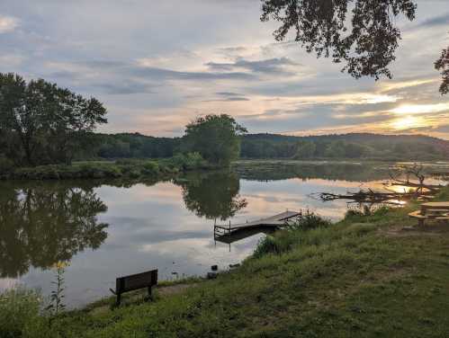 A serene river scene at sunset, with a bench and dock by the water, surrounded by lush greenery and soft clouds.