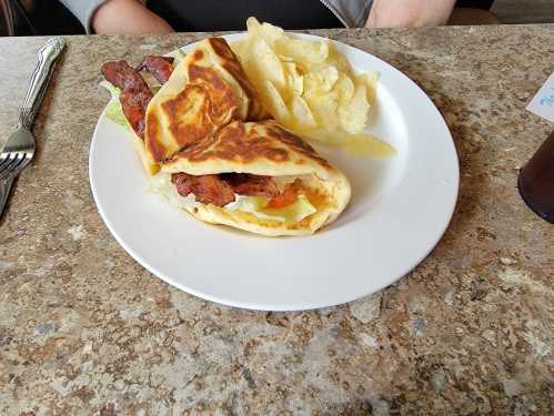 A plate with a wrapped sandwich filled with meat and vegetables, accompanied by a side of potato chips.