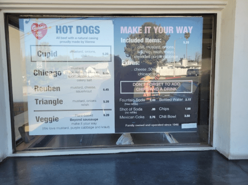 Menu board displaying hot dog options and prices, including extras and drink choices. Family-owned since 1946.