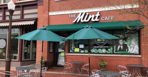 Exterior of The Mint Cafe with green umbrellas over outdoor seating and a brick facade.