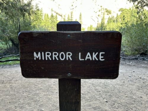 Wooden sign reading "Mirror Lake" in a natural setting with trees in the background.