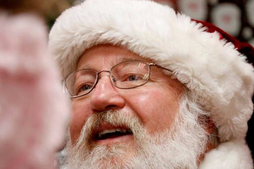 A close-up of a smiling Santa Claus wearing glasses and a fluffy red and white hat, with a joyful expression.