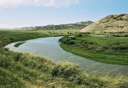 A winding river flows through a lush green landscape, surrounded by rolling hills under a clear blue sky.