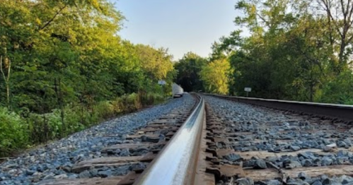 A view of a railway track curving through a lush green landscape under a clear blue sky.