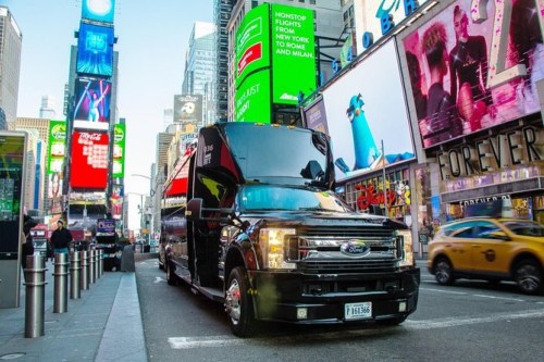 A black Ford truck parked in Times Square, surrounded by bright advertisements and yellow taxis.
