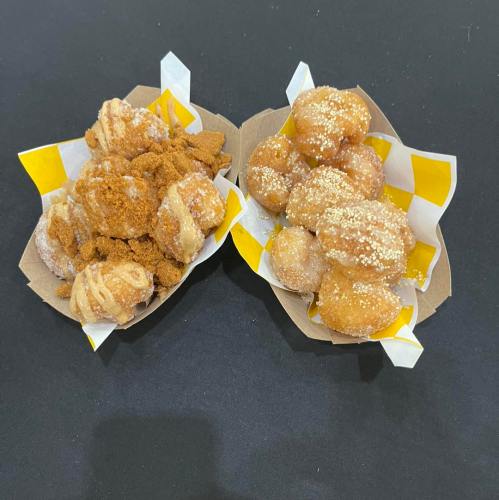 Two baskets of sweet dough balls, one coated in cinnamon sugar and the other in powdered sugar, on a black background.