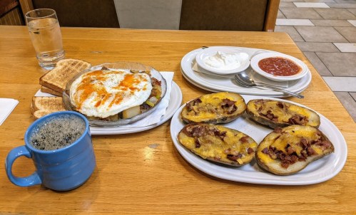 A hearty breakfast featuring a plate of eggs, toast, and a side of cheesy bacon potatoes, with coffee and water.