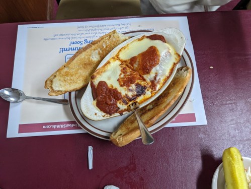 A dish of baked pasta with marinara sauce and melted cheese, served with toasted bread on a table.