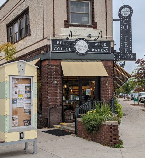 A cozy bistro with a sign for coffee, beer, wine, and bakery items, featuring a charming brick exterior.