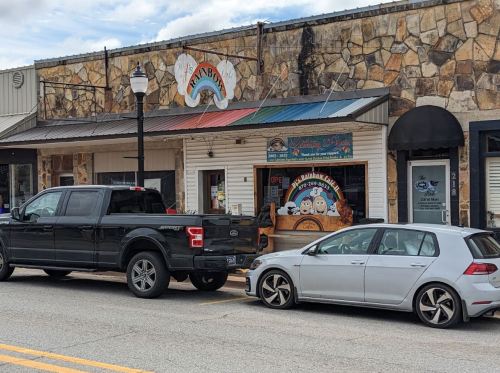 A black pickup truck and a silver car parked outside a colorful storefront with a sign that reads "Rainbow."
