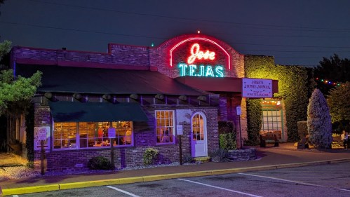 A brightly lit restaurant exterior at night, featuring a neon sign that reads "Jose Tejas" and colorful outdoor decor.