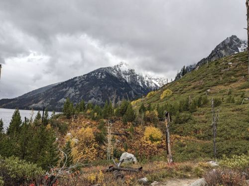 A scenic view of mountains with snow-capped peaks, lush greenery, and autumn foliage under a cloudy sky.