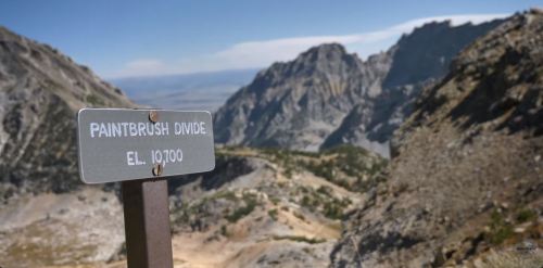 Sign marking Paintbrush Divide at 10,700 feet, with rugged mountains and a clear blue sky in the background.