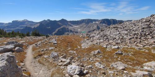 A rocky trail winds through a mountainous landscape under a clear blue sky.