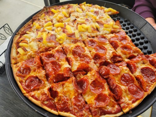 A large pizza divided into two halves: one with pepperoni and the other with ham and pineapple.