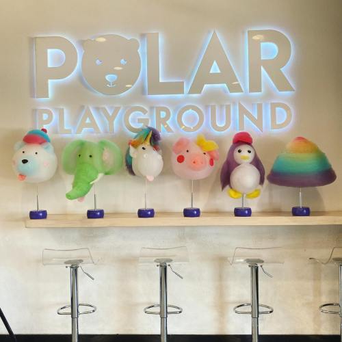 Colorful plush toys of a bear, elephant, unicorn, pig, penguin, and rainbow sit on a counter beneath a "Polar Playground" sign.