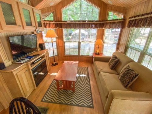 Cozy living area with a sofa, coffee table, and large windows letting in natural light. Wood paneling and decor.