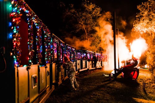 A decorated train with colorful lights at night, with smoke and flames in the background, creating a festive atmosphere.