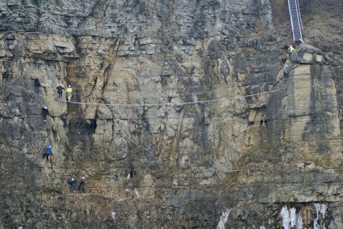 A group of climbers navigating a rocky cliff, with some using a rope bridge and others climbing the rock face.