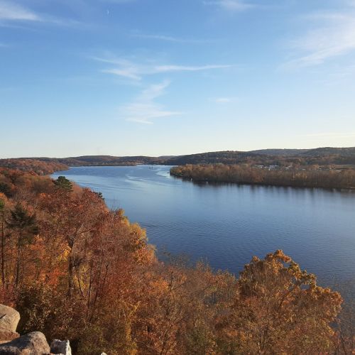 A serene river flows through a landscape of autumn trees, showcasing vibrant fall colors under a clear blue sky.