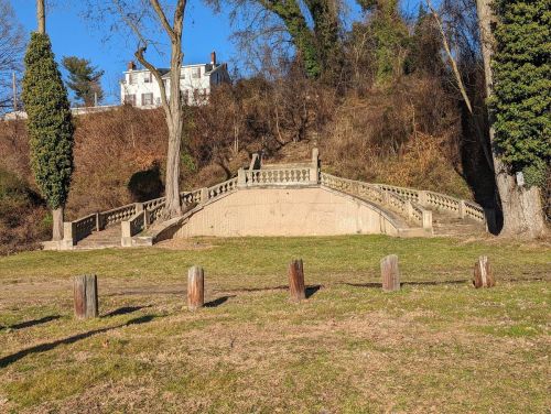 A grassy area with a stone staircase leading up to a house, surrounded by trees and wooden posts.