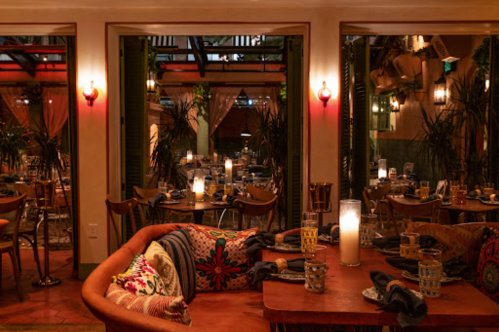 Cozy restaurant interior with warm lighting, plants, and colorful decor, featuring tables set for dining.