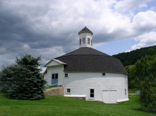 A round white building with a cupola, surrounded by green grass and trees, under a cloudy sky.