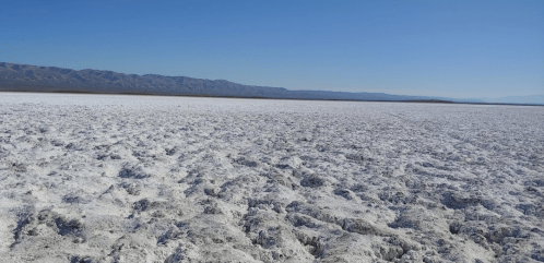 A vast, white salt flat stretches under a clear blue sky, with distant mountains on the horizon.