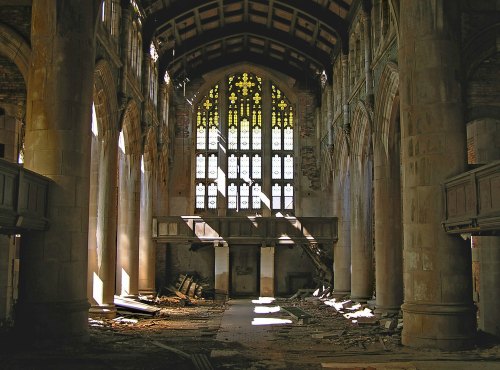 Interior of an abandoned church with tall stained glass windows, sunlight streaming through dust and debris on the floor.