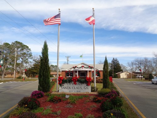 Sign for Santa Claus, Georgia, with flags and festive decorations, surrounded by colorful flowers and greenery.