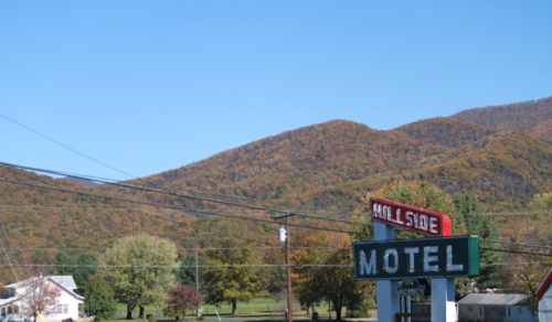 A hillside motel sign in front of colorful autumn mountains under a clear blue sky.