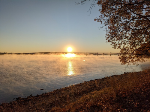 Sunrise over a misty river, with golden light reflecting on the water and trees framing the scene.