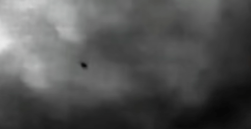 A small dark object is visible against a cloudy, gray background.