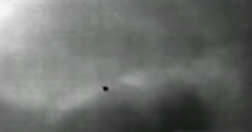 A blurry, monochrome image showing a small, dark object against a cloudy background.
