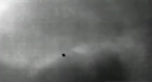 A small, dark object is seen against a cloudy, gray background, suggesting an unidentified flying object.