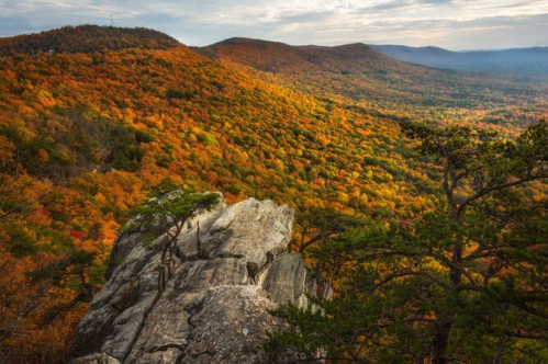 A rocky outcrop overlooks a vibrant autumn landscape filled with colorful trees and rolling hills.