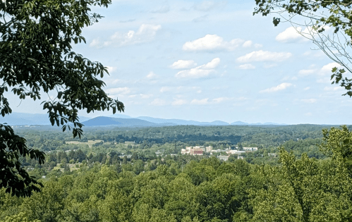 A panoramic view of lush green hills and distant mountains under a partly cloudy sky.