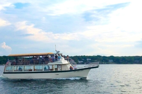 A tour boat filled with passengers sails on calm waters under a cloudy sky.